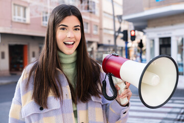 Young Brazilian woman at outdoors holding a megaphone and with surprise expression