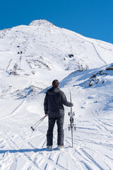 Fototapeta na wymiar Skier holding his skis in the middle of the snowy mountain looking at the highest peak