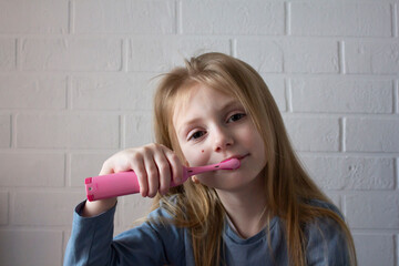 blonde girl brushing her teeth against a white wall
