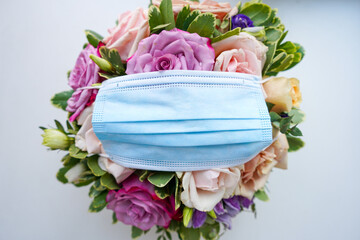 Protective surgical mask with arranged flowers on white background. Creative spring, bloom, covid-19 or coronavirus layout. Flat lay, top view.