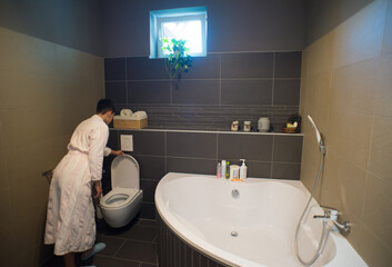 Woman in bathrobe going to the toilet in the modern bathroom.