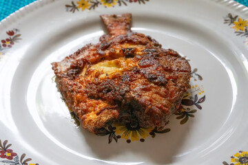 A fried pomfret fish served on a white decorated platter, Spicy Indian food. Pomfrets are perciform fishes belonging to the family Bramidae.
