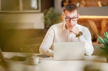 Serious attentive focused businessman sits in the office at a large table in front of a laptop and works online, video chat, communication on working moments on the Internet, work from the office