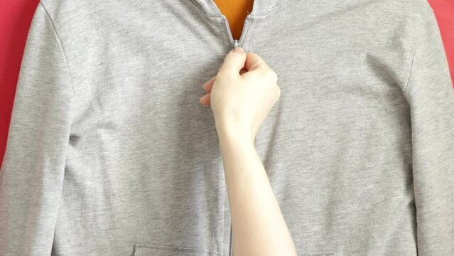 zipper on the clothes is unfastened by female hands, under it is an orange T-shirt