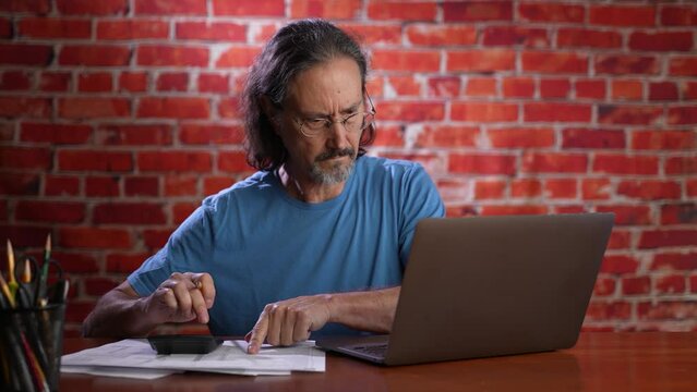 Stressed pensive thoughtful focused casual business accountant bookkeeper in office looking at and working with laptop and income tax return papers and documents