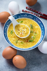 Bowl of chinese traditional egg-drop soup or danhuatang, vertical shot on a light-blue stone surface