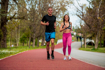 Obraz premium Woman and man jogging on red path in the city park together