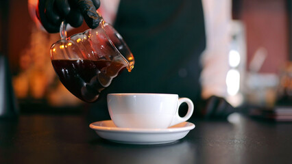 Pouring Black Coffee In Cup. Waiter pouring coffee into a white cup in a restaurant.