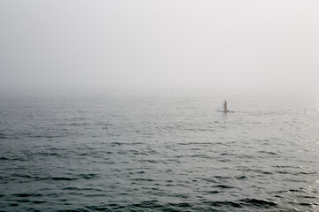 A man surfing in the fog on the sea in the distance.