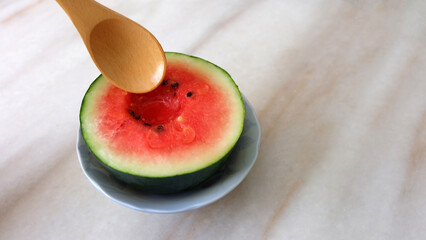 Wooden spoon trying to dig into a small watermelon cut in half. With copy space on the right.