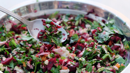 A bowl of fresh and raw vegetable chop, with coriander leaves, pak choy, carrot and beetroot. With a metal spoon scooping out some of the vegetable mix.