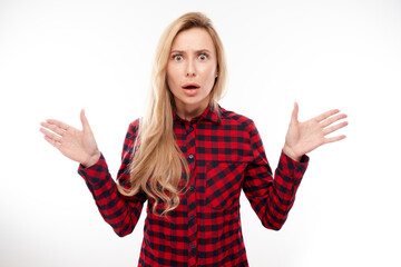 Shocked blond girl looks surprised spreads her arms on white studio background with copy space