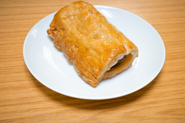 A fresh from the oven homemade rustic sausage roll on a white plate