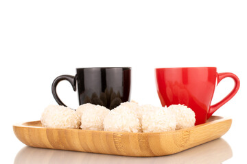 Some sweet coconut candy on a bamboo tray with two cups, macro, isolated on a white background.