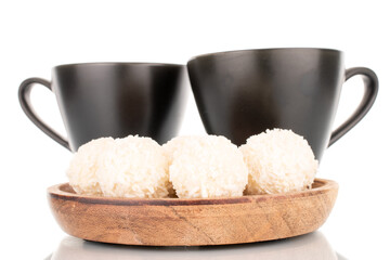 Some sweet coconut candy on a wooden saucer with two cups, macro, isolated on a white background.