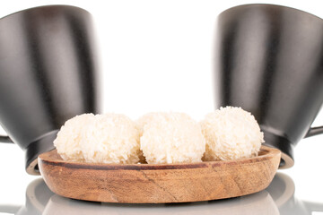 Some sweet coconut candy on a wooden saucer with two cups, macro, isolated on a white background.