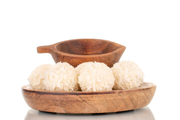 A few sweet coconut candies on a wooden saucer with a wooden cup, macro, isolated on a white background.