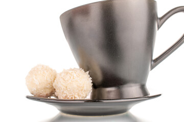 Two sweet coconut candies on a saucer with a black cup, macro, isolated on a white background.