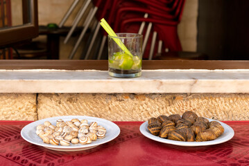Two plates with different snails and a glass of caipirinha