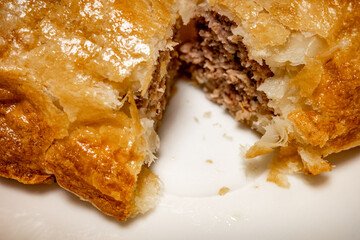Close up of a fresh from the oven homemade rustic sausage roll cut in half on a white plate with intentional shallow depth of field and soft focus