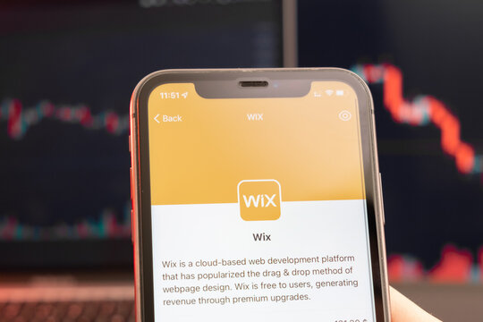 Wix stock price decrease on the trading market with downtrend line graph bar chart on the background. Man holding a mobile phone with company logo, February 2022, San Francisco, USA. 
