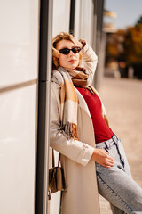 student or businesswoman in sunglasses and a coat with scarf walks down a street