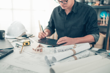 Mini model house on blueprint plan while architector working on tablet background. House Architect...