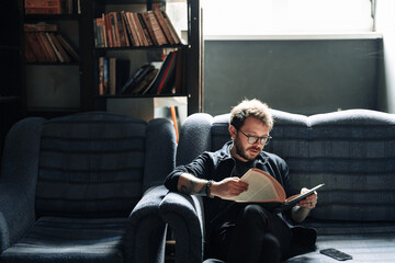 Adult student reading a book in the college library. Young positive male wearing glasses with...