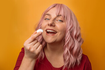 Happy woman holding white marshmallow in hand over yelow wall background. Sweets, confectionery and...