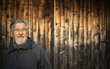 Senior man enjoying the outdoors, hiking, walking throught lovely nature, standing in front of a wooden chalet