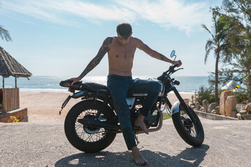 Fototapeta na wymiar Young shirtless caucasian guy with full-arm tattoo sitting on motorcycle