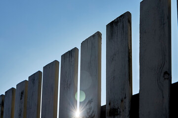 Wooden gray fence on a sunny summer day. The sun shines through the wooden fence.