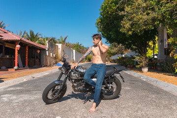 Young shirtless caucasian man with full-arm tattoo sitting on motorcycle