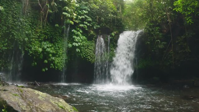 A beautiful view of natural waterfall in the middle of nowhere. Tropical paradise scene. Jungle of Indonesia with river cascade. Rainforest landscape on a cute lake with waterfall. Slow motion. 4k.