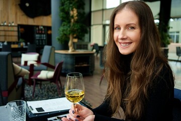 Portrait of woman sitting in restaurant, drinking and tasting wine, smiling.