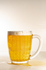 The glass mug is filled with fresh, light beer, with a thick foam. Beer glass with beer and thick foam, with a light background.