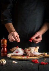 Chef prepares raw chicken legs in the restaurant kitchen. The cook puts red viburnum berries on a chicken leg before baking. National dish