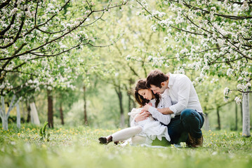 Mom and dad with baby daughter or son, young family outdoors in spring against the background of blooming apple and cherry trees. Happy parents in blossom garden.