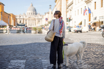 Stylish woman walks with a dog on the street on background of saint Peter's cathedral in Rome....