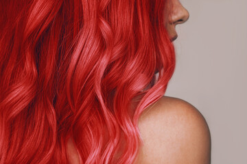 Close-up of the wavy hot red hair of a young woman isolated on a beige background. Result of coloring, highlighting, perming. Beauty and fashion