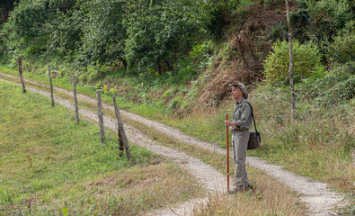 Pilgrim with hat, bag and stick walking along a path through the countryside on the Camino de Santiago. Way of St James