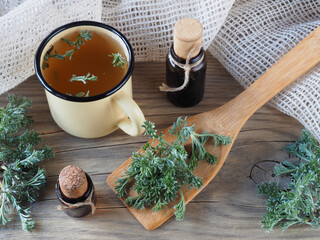 Fresh young wormwood leaves, oil, tincture and herbal  tea, napkin on a wooden background, flat...