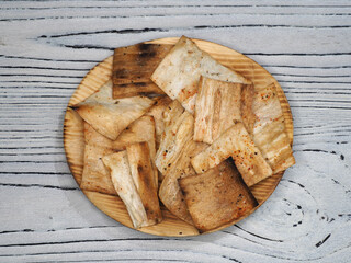 Natural fried lavash chips in a plate on a light wooden background, top view, flat layout. Delicious quick snack from pita bread for diet food