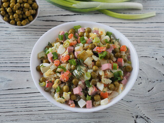 Recipe for vegetable salad olivier with salted cucumbers, canned peas in bowls and green onions on a white wooden table, flat layout, selective focus. Russian cuisine