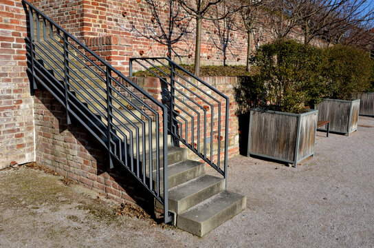 stairs and railings of exposed brick smooth surface. Metal railings and benches in the corners of the U-shaped brick retaining walls. The recessed lights illuminate the pedestrians' feet under  feet