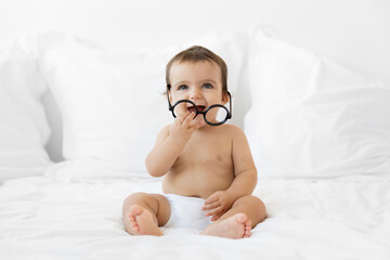 Smiling baby girl holding eyeglasses while sitting on bed