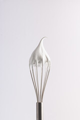 Meringue. Confectionery whipped cream on a whisk. Close-up of a shiny metal whisk with a tip of...