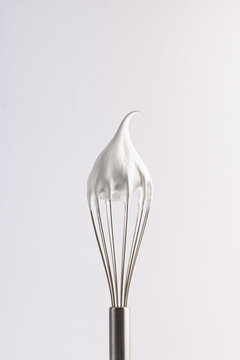 Meringue. Confectionery whipped cream on a whisk. Close-up of a shiny metal whisk with a tip of meringue, emphasizing texture and quality on a white background.