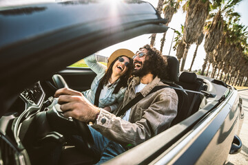 Happy couple driving convertible car enjoying summer vacation - Friends rent cabrio auto on holiday - Roadtrip, freedom, travel and transport rental service concept - obrazy, fototapety, plakaty