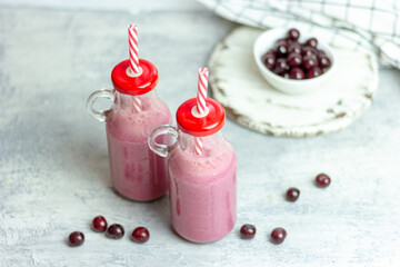A bottle of cherry smoothies on a white background, cherries in bulk and in a plate. Morning summer breakfast